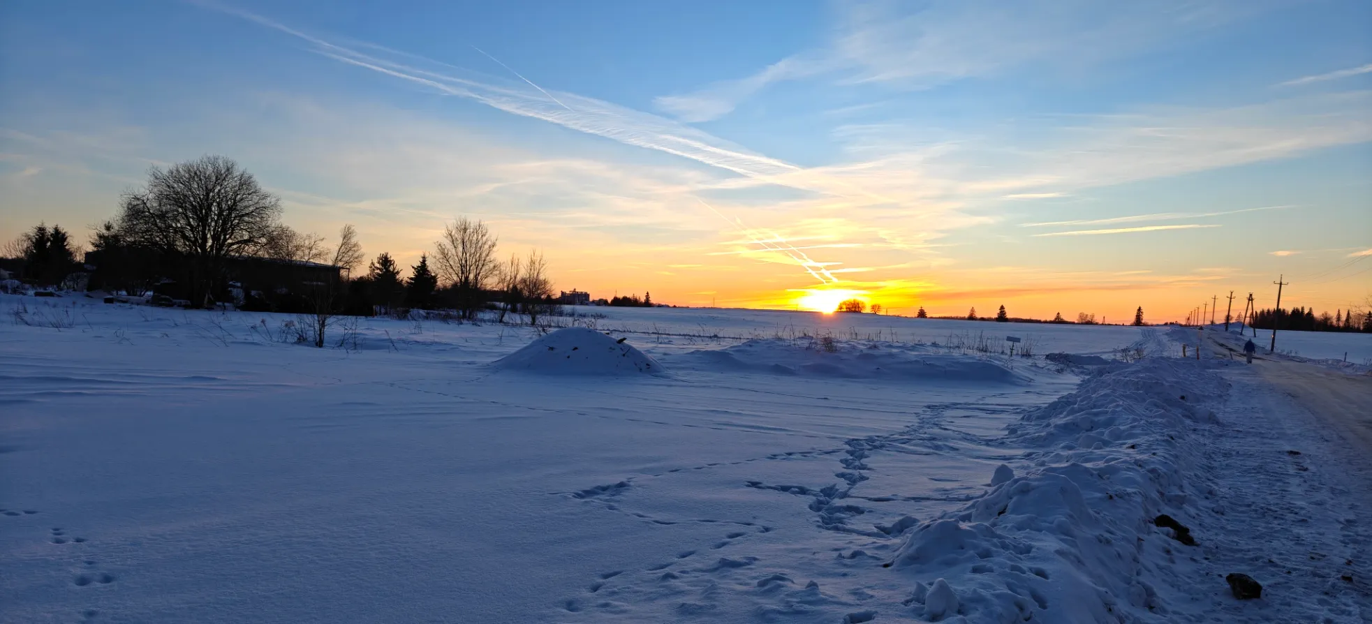 Photo d'une campagne sous la neige au coucher de soleil, sur la droite une route longe
les champs